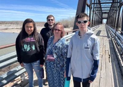 Four individuals stand on a bridge, overlooking a serene river flowing in the background